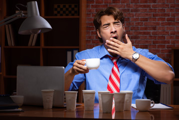Young employee drinking coffee working at night shift 
