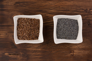 Poppy and flax seeds in a ceramic plates on wooden table background. Selective focus