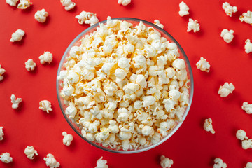 Glass bowl of salty popcorn on a red background. Top view with copy space. Flat lay