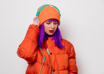 Portrait of a beautiful girl with purple hair in orange hat and jacket and with headphones on white background. Trendy style