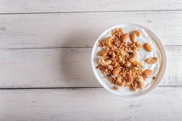 White plate with greek yogurt, granola, almond, cashew, walnuts  on white wooden background.