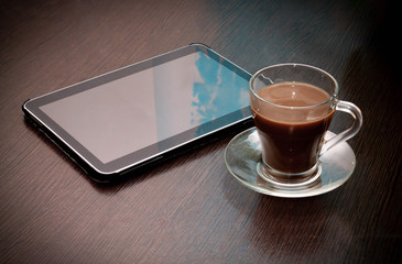Fototapeta na wymiar black coffee with milk in a Cup and a tablet with the sky reflected in it lie on a wooden table