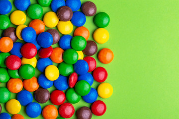 Fototapeta na wymiar Glazed colored chocolate candies are gathered on bright green background