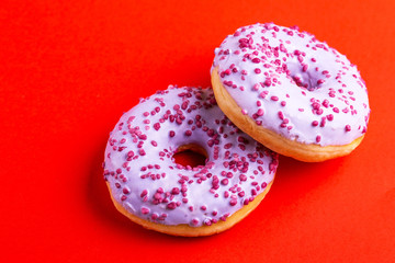 Two delicious lilac donuts with sprinkle on bright red background