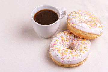Two delicious vanilla donuts with sprinkle and cup of coffee