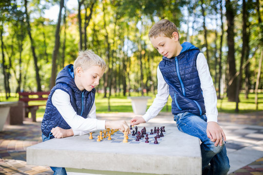 The topic is children learning, logical development, mind math, miscalculation moves advance. Big family two brothers Caucasian boys playing chess in the park in bright sunny weather in the autumn