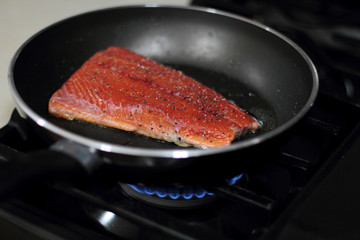 Wild caught Coho salmon frying in a pan with the skin side down.