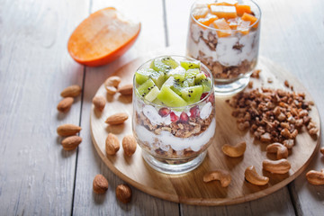 dessert with greek yogurt, granola, almond, cashew, kiwi and persimmon on white wooden background.