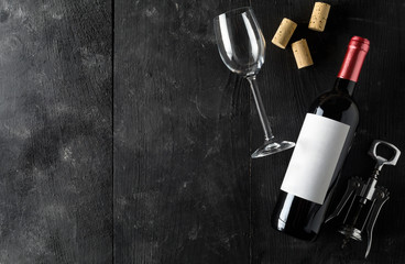 Red wine bottle with corkscrew, corks and wine glass on dark wooden table flat lay from above