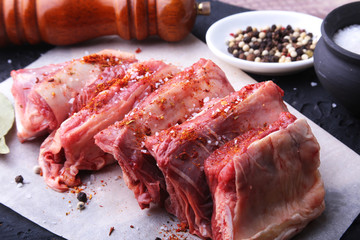 Raw fresh meat, uncooked lamb or beef ribs with pepper, garlic, salt, bay leaves and spices on dark stone background, Ready for cooking. copy space.
