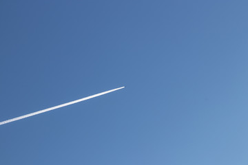 Lone airplane with soft white trail amidst stark blue sky
