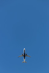 Lone airplane with soft white trail amidst stark blue sky