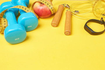 Fitness concept with blue dumbbells, jump rope and fitness tracker on a yellow background, copy space
