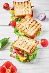 Three sandwiches with ham, lettuce and fresh vegetables on a white background - obrazy, fototapety, plakaty