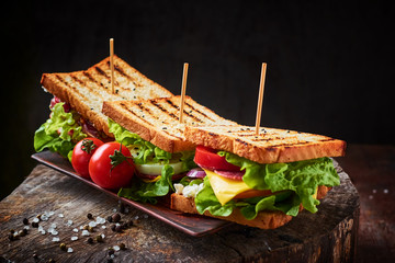 Homemade sandwich with ham, lettuce, cheese and tomato on a wooden background