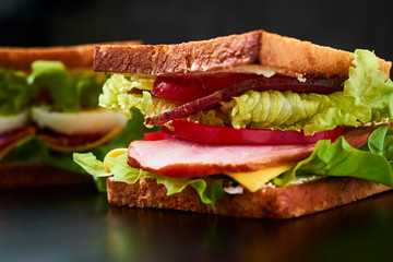 Homemade sandwich with lettuce and ham on a black background, close up