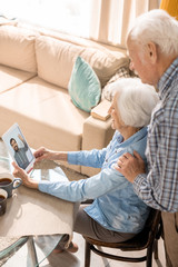 High angle portrait of modern senior couple using digital tablet and smiling while video chatting with son at home