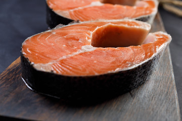 Salmon steak on wooden plate on black
