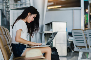 Beautiful asian woman teenager using laptop computer at airport terminal sitting with luggage suitcase and backpack for travel in vacation summer relaxing waiting flight transport