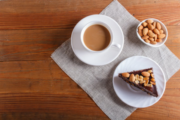 Chocolate cake with caramel, peanuts and almonds on a brown wooden background.