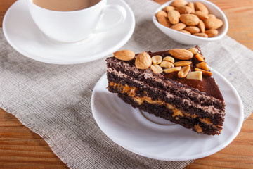 Chocolate cake with caramel, peanuts and almonds on a brown wooden background.