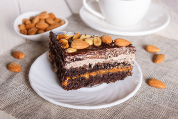 Chocolate cake with caramel, peanuts and almonds on a white wooden background.
