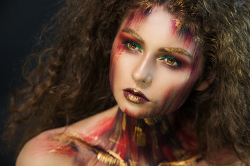 Fototapeta premium beautiful curly girl in a fire makeup and green shadows under the cloak image created by a make-up artist