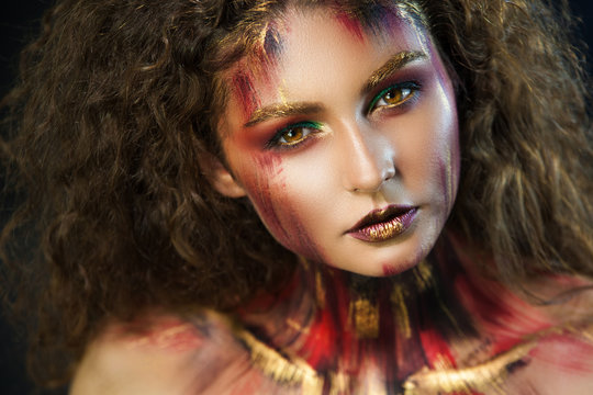 beautiful curly girl in a fire makeup and green shadows under the cloak image created by a make-up artist