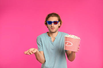 Emotional man with 3D glasses and popcorn during cinema show on color background