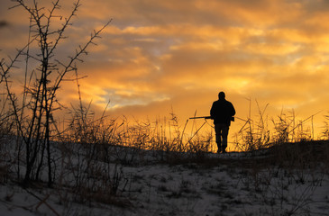 Winterjagd bei Sonnenaufgang. Jäger, der sich mit Schrotflinte bewegt und nach Beute sucht.