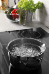 Pot with boiling water on electric stove in kitchen, space for text