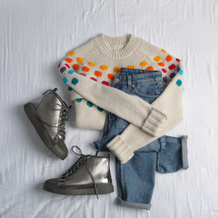 Flat lay composition with jeans, sweater and shoes on white fabric