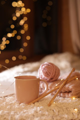 Composition with cup of hot beverage and knitting yarn on fuzzy rug. Winter evening