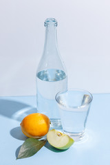 A bottle of water, a glass and a green apple on a blue background. Minimalistic concept.