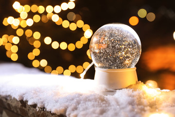 Snow globe and blurred Christmas lights on background. Space for text