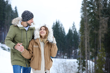 Obraz premium Happy couple near conifer forest on snowy day, space for text. Winter vacation