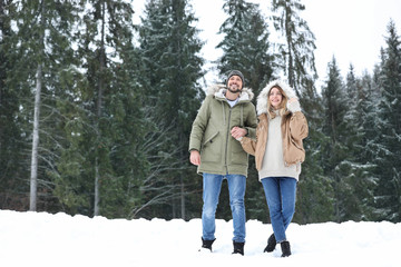 Fototapeta na wymiar Couple near conifer forest on snowy day, space for text. Winter vacation