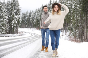 Obraz premium Couple walking near snowy forest, space for text. Winter vacation
