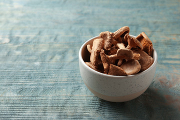 Bowl of dried mushrooms on color wooden background. Space for text
