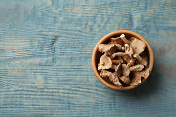 Bowl of dried mushrooms on color wooden background, top view with space for text