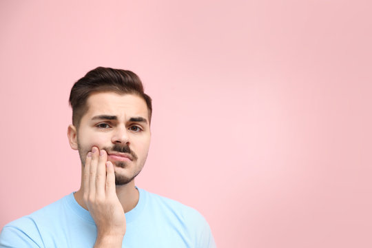 Young man suffering from strong tooth pain on color background, space for text