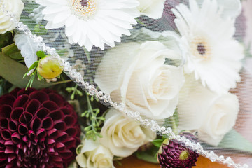 Fototapeta na wymiar Wedding veil over bridal bouquet of dahlia, roses, and white gerberas