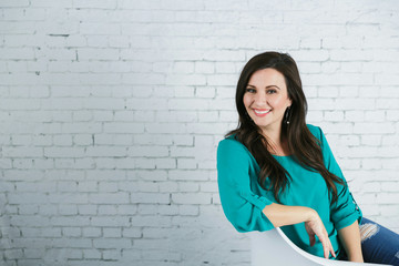 Beautiful Hispanic Woman Sitting Against White Brick Wall