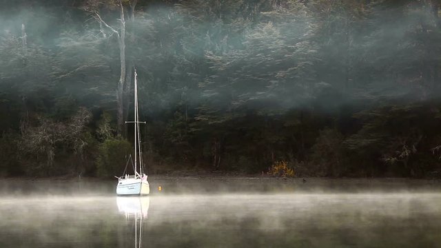 Sail boat at the lake on a foggy misty winter morning. Very calm scene with moving fog