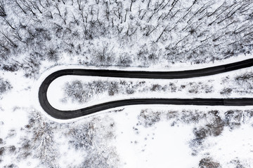 Aerial view of a beautiful serpentine road surrounded by a forest of pine trees and white snow. National Park of Abruzzo, Lazio and Molise, Italy.
