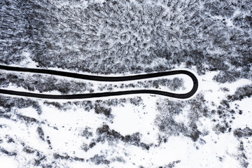 Aerial view of a beautiful serpentine road surrounded by a forest of pine trees and white snow....