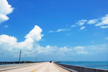 Empty highway in Miami in clear weather with lots of white fluffy clouds and ocean views. Florida's summer road across the bridge with a balanced flow of cars