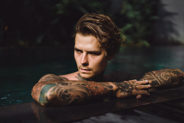 young handsome man in tattoos resting in the outdoor pool. A tattooed man in the pool is having fun. on bali, indonesia