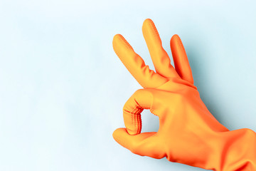 Fototapeta na wymiar Female hand in orange rubber gloves shows ok sign, blue background