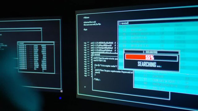 Computer hacker finished uploading software on one of his dual screens in the dark